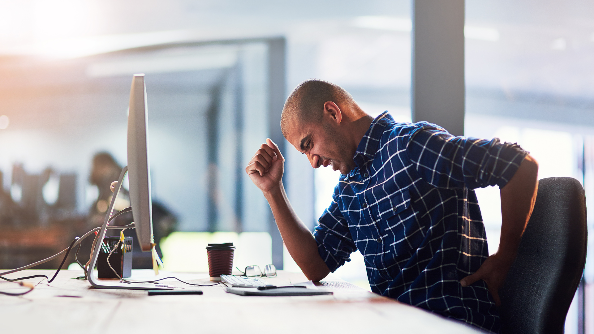 An image of a man at work suffering from back pain due to poor seating posture